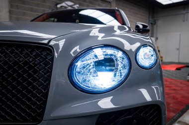 Gri Bentley Bentayga 'nın yakın görüntüsü dairesel LED farlar, siyah ızgara ve kapalı bir sergi salonunda cilalı bir yüzey..