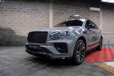 Gri Bentley Bentayga lüks SUV, siyah ızgara ızgara ve alaşımlı tekerlekler, kareli bir zemine park edilmiş beton duvarlı ve klimalı bir sergi salonunda.