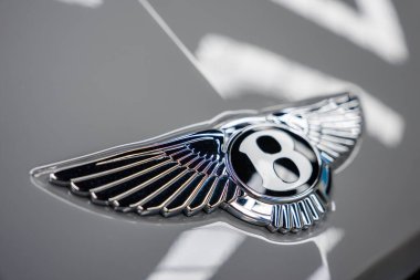 Bentley logosunun parlak bir yüzeyde gümüş bir B ve genişleyen kanatlar içeren detaylı görüntüsü, karmaşık tasarım ve işçilik içeriyor..