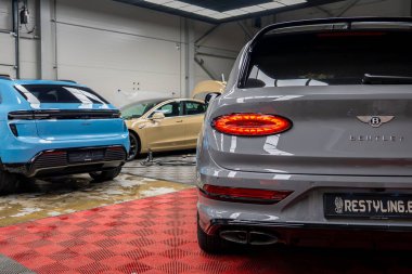 Gri Bentley Bentayga, parlak arka ışıkları, mavi Porsche Macan ve bej renkli Lamborghini Urus, kırmızı kareli döşemeleriyle iyi aydınlatılmış bir galeride..