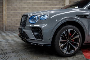 Bentley Bentayga marka gri bir jipin ön tarafı. Özel bir ızgarası, yuvarlak farları, kırmızı fren kalibreleri ve kapalı bir alanda alaşımlı tekerlekleri var..