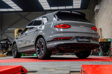 Gümüş Bentley Bentayga lüks SUV kırmızı ve gri fayanslı zemin üzerinde iyi aydınlatılmış bir garajda araç gereç, ekipman ve depo görünür.