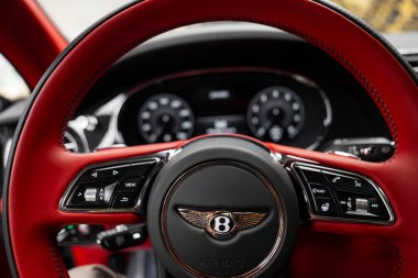 Kırmızı deri süslemeli Bentley direksiyon, Bentley logosu, cilalanmış metal aksanlar ve arka planda parlak bir gösterge paneli..