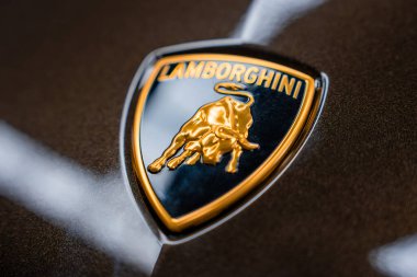 Lamborghini ambleminin detaylı bir görüntüsü altın aksanlı siyah bir kalkandaki altın bir boğayı yansıtan koyu metalik bir yüzeye karşı koyuyor..