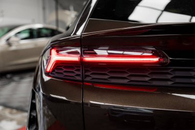 Porsche Macan 'ın kırmızı LED arka lambasının detaylı görüntüsü iyi aydınlatılmış bir kapalı alanda, arka planda bulanık bej bir araba ile.