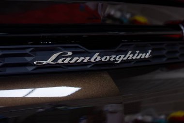 Siyah bir bal peteği ızgarasında gümüş amblem olan Lamborghini 'nin arka kısmı. Parlak yüzey bulanık arkaplan ile ışığı yansıtır.