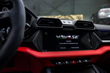 Lamborghini Urus 'un kırmızı deri aksanlı gösterge panelini kapat ve başka bir arabanın kapalı arka planını bulanıklaştır..