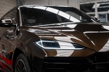 Lamborghini Urus 'un açılı farlarını, parlak kahverengi dış görünüşünü ve kapalı bir galeride yansımalarını yakından görebiliriz..
