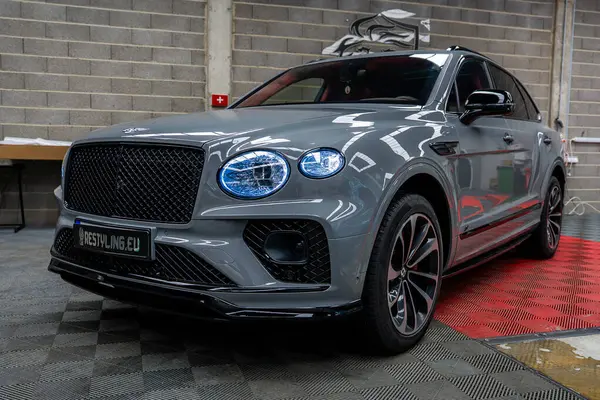 Lüks Bentley Bentayga SUV gri kaplamalı, siyah ızgara ve alaşımlı tekerleklerle Avrupa otomobil galerisinde kareli bir zemine park edilmiş..