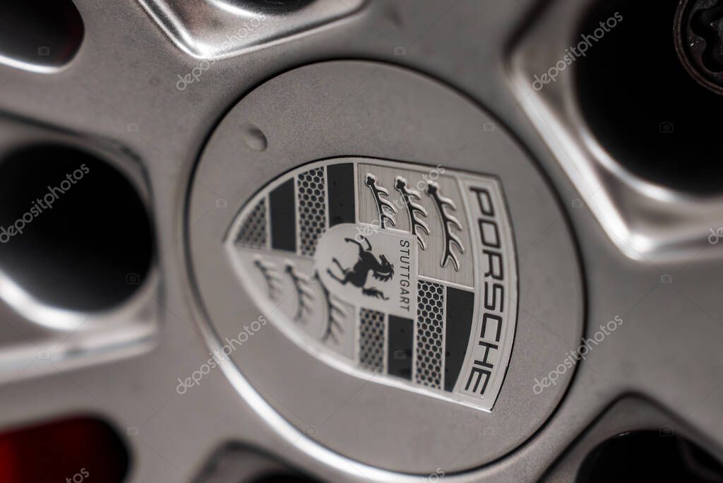 Detailed view of the Porsche emblem on a car wheel, showcasing the crest with black, red, and gold elements against a polished silver background.
