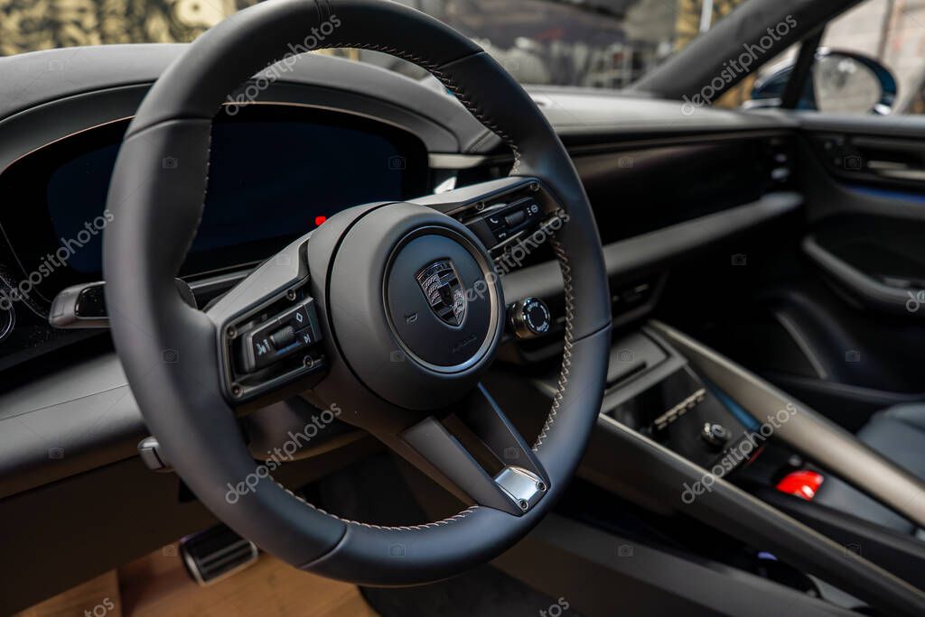 Close up of a Porsche interior showing the black leather steering wheel with logo, detailed stitching, and a sleek dashboard with digital displays.