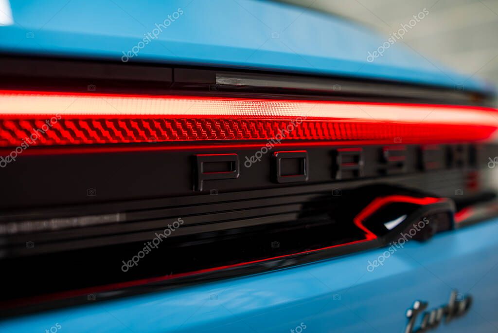Rear view of a blue Porsche showcasing the illuminated red LED taillight bar, black Porsche lettering, and partially visible silver Turbo badge.