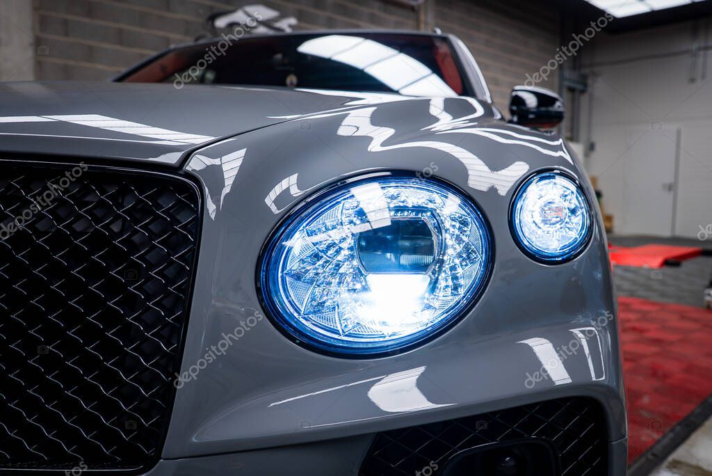 Close up view of a gray Bentley Bentayga showcasing circular LED headlights, black mesh grille, and polished surface in an indoor showroom setting.