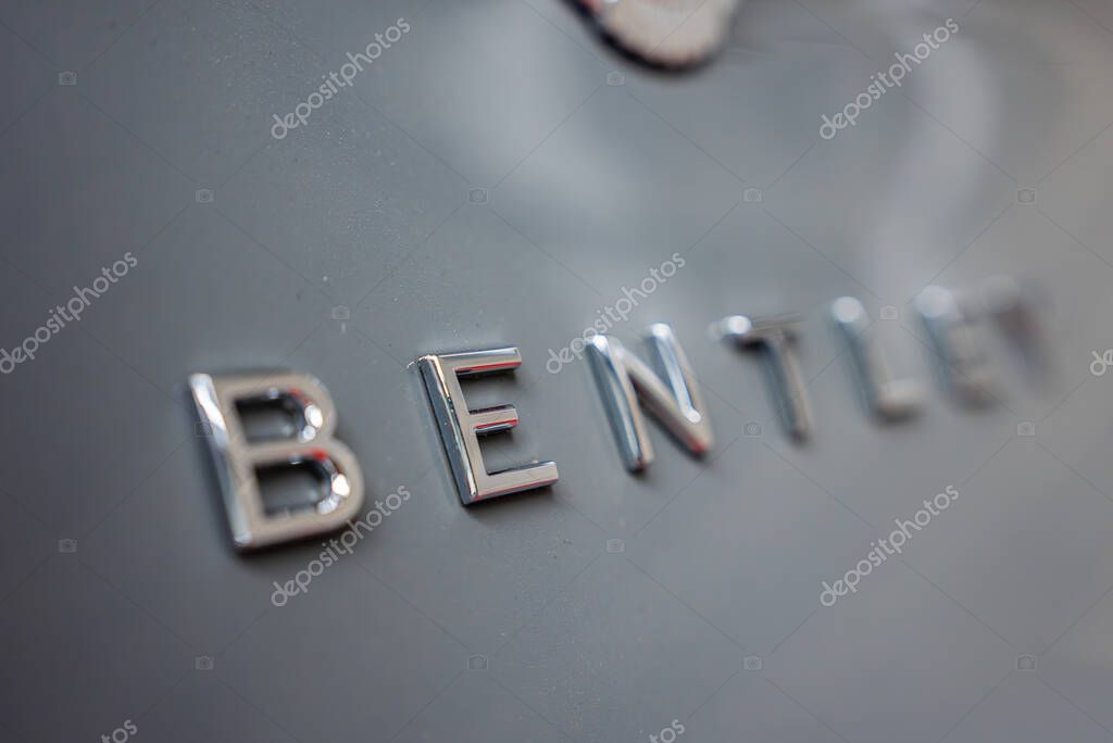 A detailed view of the chrome Bentley emblem on a glossy surface, with sharp focus on the lettering and a blurred background emphasizing luxury design.