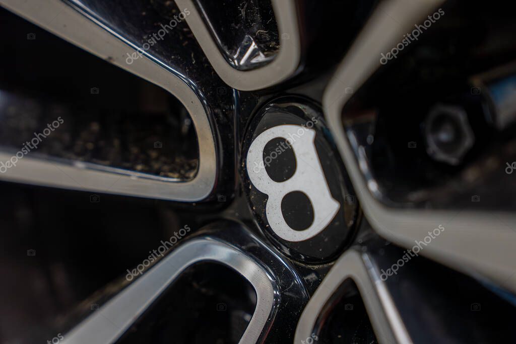 Close up view of a Bentley wheel center cap featuring the iconic B logo, polished metallic spokes, and a glossy black finish with visible dirt details.