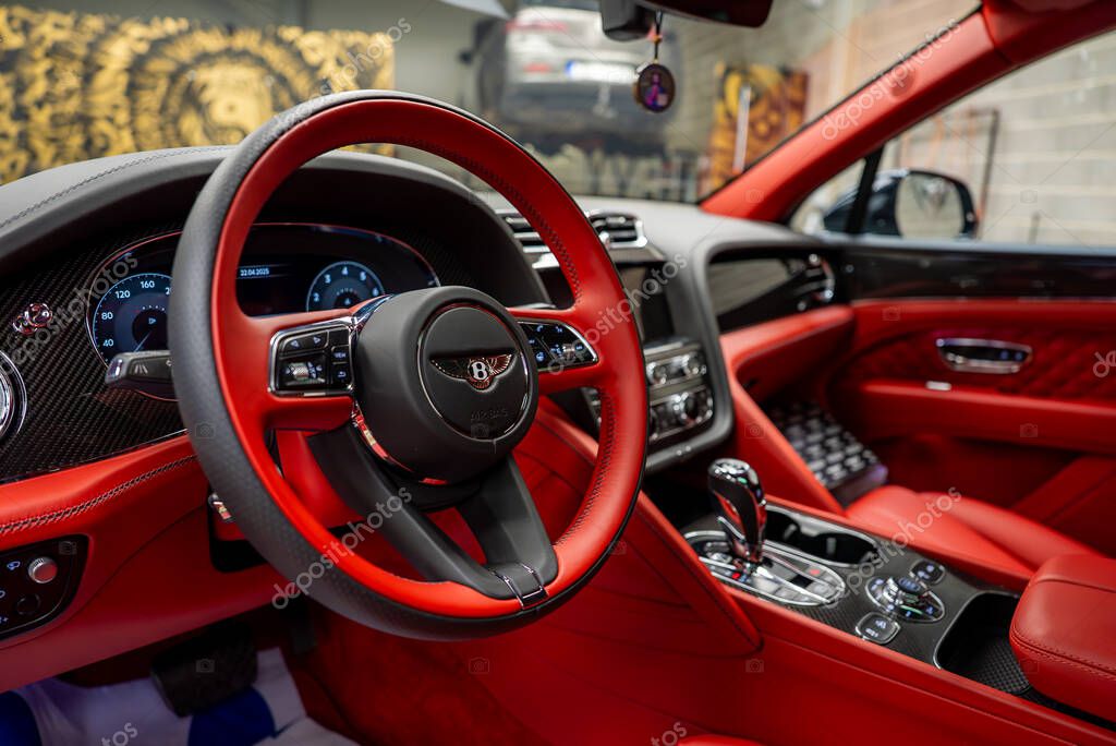 Luxurious red leather interior of a Bentley Bentayga, featuring intricate stitching, digital dashboard, chrome accents, and a high end showroom setting.