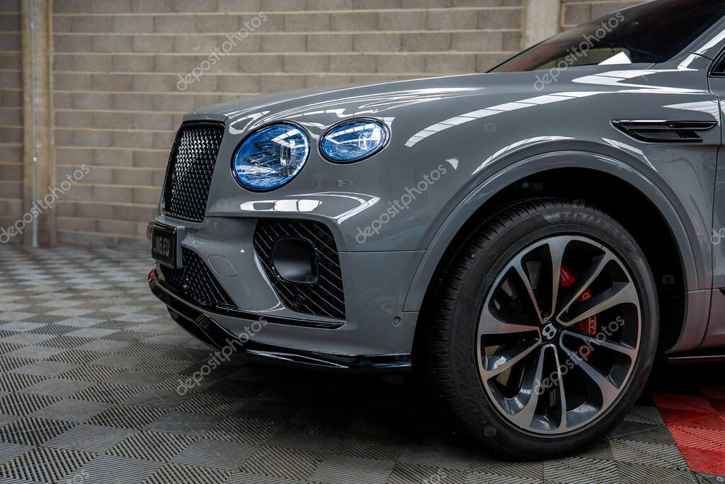 Front section of a gray Bentley Bentayga SUV with a distinctive grille, round headlights, red brake calipers, and alloy wheels in an indoor space.