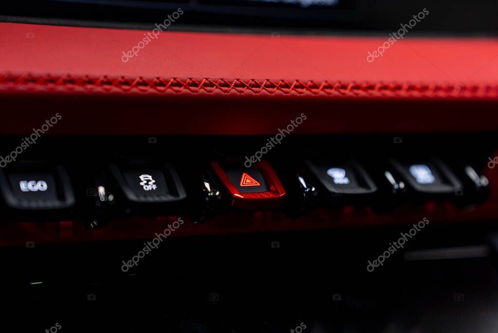 Close up view of a luxury car's control panel featuring a red hazard light button, advanced driving controls, and red leather with detailed stitching.