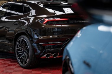 Siyah Lamborghini Urus 'un arka tarafında dört egzoz boruları ve özel stop lambaları vardı. Bir galerinin kırmızı kareli zeminine park edilmişti. Mavi bir araba kısmen görünür..