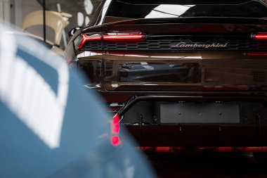 Siyah bir Lamborghini Urus 'un arkası. Işıklı stop lambaları ve logosu var. Kapalı, yansıtıcı yüzeyleri ve ön planda bulanık lüks bir arabası var..