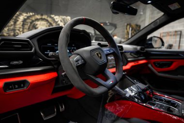 Lamborghini Urus 'un içinde siyah ve kırmızı Alcantara direksiyon simidi, dijital gösterge paneli ve modern endüstriyel arka plan var..