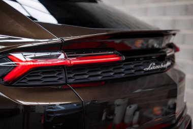 Lamborghini Urus arka bölümünün kapalı görüntüsü, parlak arka ışık tasarımı, metalik kahverengi boya ve siyah süslemeli Lamborghini logosu..