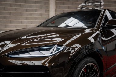 Lamborghini Urus 'un ön bölümünün yakın görüntüsünde açısal farlar, alaşımlı tekerlekler ve kapalı bir alanda metalik bir boğa heykeli var..