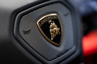 Lamborghini logosuna yakından bak. Siyah bir kalkanda altın bir boğa var. Dokulu yüzey ve bulanık kırmızı detay görsel derinlik ekler.