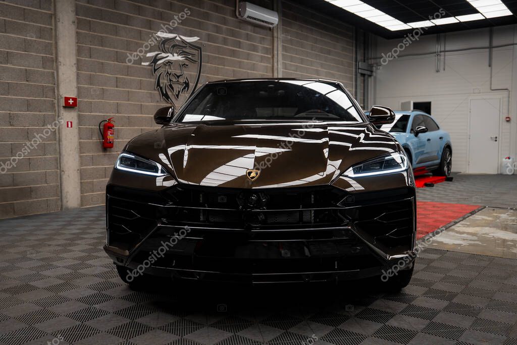 Black Lamborghini Urus parked indoors on a checkered floor with a lion emblem on the wall, a blue Porsche Macan in the background, and industrial decor.