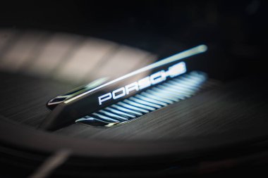 Fırçalanmış metalik bir yüzeyde parlayan Porsche logosunun yakın görüntüsü 2025 Porsche 911 GT3 922 'nin modern tasarım ve işçiliğini gözler önüne seriyor..