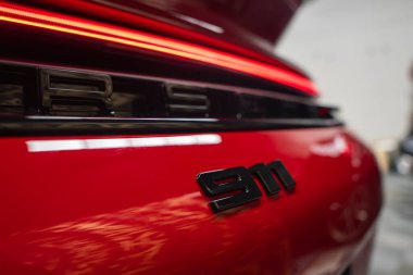 Kırmızı 2025 Porsche 911 GT3922, siyah 911 rozeti, yatay aydınlatma çubuğu ve kapalı alanda parlak yansıtıcı bir kapsama alanı var..