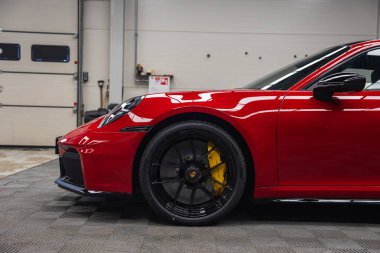 Kırmızı bir 2025 Porsche 911 GT3922 'nin ön tarafı siyah alaşımlı tekerlek, sarı fren kalibreleri ve kapalı bir garajda parlak bir tasarım odaklı..