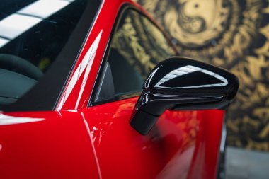 2025 model kırmızı bir Porsche 911 GT3922 'nin yan aynası ve kapısı. Parlak siyah aksanlı. Yansımalar ve altın soyut duvar resmi modern tasarımı geliştirir..