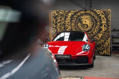 Kırmızı bir 2025 Porsche 911 GT3922, Yin Yang sembollü, döşemeli ve atölye ekipmanlı altın ve siyah bir arkaplan karşısında sergilendi..