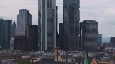 Frankfurt, Almanya 'nın hava manzarası, Commerzbank Kulesi gibi gökdelenler, geleneksel çatılar, ve bulutlu bir gökyüzü altında ağır çekimde vinçler.