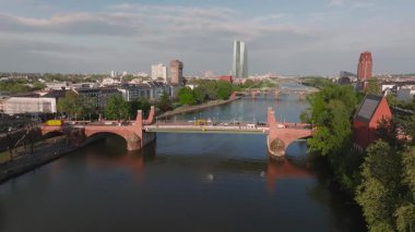 Frankfurt, Almanya 'nın havadan görünüşü, Ana Nehir' i gösteriyor, kırmızı tuğlalı bir köprü, hareket eden tekne, araçlar, modern ve geleneksel binalar, ve yeşil alanlar.