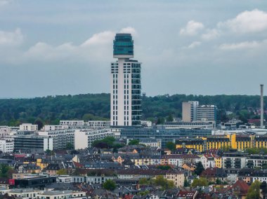 Frankfurt, Almanya 'nın havadan görünüşü, silindirik cam kapaklı, kentsel konutlar, yeşillikler ve bulutlu gökyüzü ile çevrili modern bir gökdeleni vurguluyor..