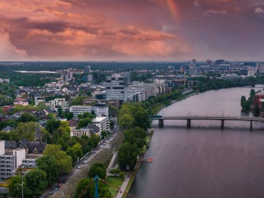 Frankfurt, Almanya 'nın hava görüntüsü, Ana Nehir, bir köprü, şehir silueti, yemyeşil yemyeşil ve soluk bir gökkuşağı ile canlı bir gün batımı.