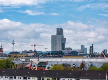 Westend Tower ve Europaturm ile Frankfurt şehir manzarası, modern ve geleneksel mimari, konut çatıları ve inşaat vinçlerinin sergilendiği.