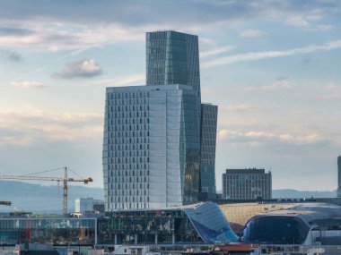 Frankfurt, Almanya 'da modern yüksek binalar tasarlandı ve cam cephe oluşturuldu. Ön planda kıvrımlı bir çatı yapısı ve inşaat vinci görünüyor..