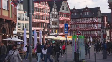 Frankfurt, Almanya 'daki Romerberg Meydanı' nda yarım keresteli binalar, açık hava oturma yerleri ve canlı bir şehir sahnesinde yürüyen ve sosyalleşen kalabalıklar yer alıyor..