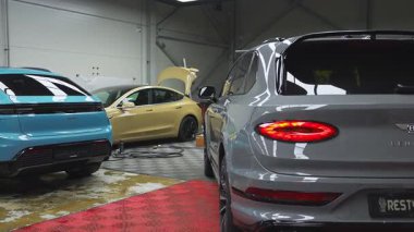 Frankfurt 'ta Bentley ve Porsche gibi lüks arabaların yer aldığı kapalı otomotiv atölyesi, kaplan duvar resmi, aletler ve araçlarla hareket eden işçiler.