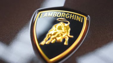 Lamborghini logosuna altın boğa amblemi ve parlak bir yüzeye yazılmış kalın bir metin ile statik yakın plan, Frankfurt 'taki metalik kaplamayı vurguluyor..