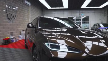 Lamborghini Urus koyu renk bir kaplama ve mavi Porsche Macan iyi ışıklandırılmış parkeleri ve endüstriyel duvarları olan bir garajda..