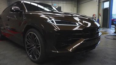 Turkuaz bir Lamborghini Urus Frankfurt 'ta lüks bir garajda kırmızı ve siyah bir paspas üzerinde, endüstriyel duvarları, cam kapısı ve kısmen görülebilen başka bir araba..