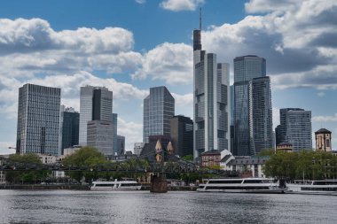 Frankfurt 'tan yükselen Commerzbank Kulesi de dahil olmak üzere modern gökdelenler. Ana nehir ve Eiserner Steg köprüsü ağaçlar ve karışık mimari tarafından çerçevelenmiştir..