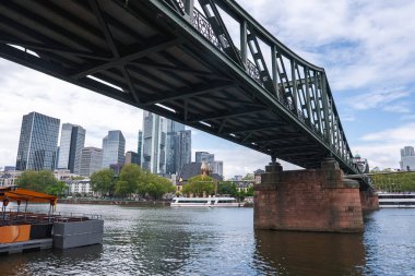Eiserner Steg köprüsü Frankfurt, Almanya 'daki Main River boyunca uzanır, yeşil demir yapısı, kırmızı taş iskeleleri ve arka planda modern gökdelenleri vardır..