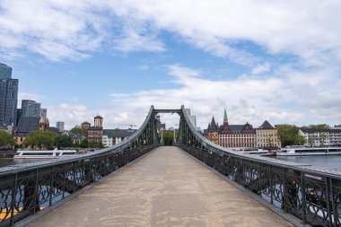 Eiserner Steg köprüsü Frankfurt, Almanya 'daki Main River' ı, süslü demirişleri, şehir gökdelenleri, bir kilise kulesi ve ağaç sıralanmış nehir kenarları ile kaplar..