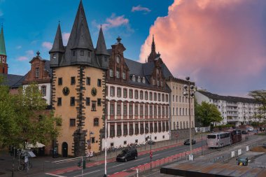 Frankfurt, Almanya 'daki Saalhof binasında, otomobiller ve otobüslerle dolu işlek bir cadde yakınındaki ortaçağ kuleleri ve saati bulunan bir mimari yer alıyor..