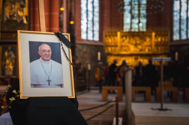 Bir Frankfurt kilisesinin içinde Papa Francis 'in çerçeveli bir fotoğrafı vardır. Siyah örtülü bir sehpada, tespih, süslü bir sunak ve boyalı cam pencereler..